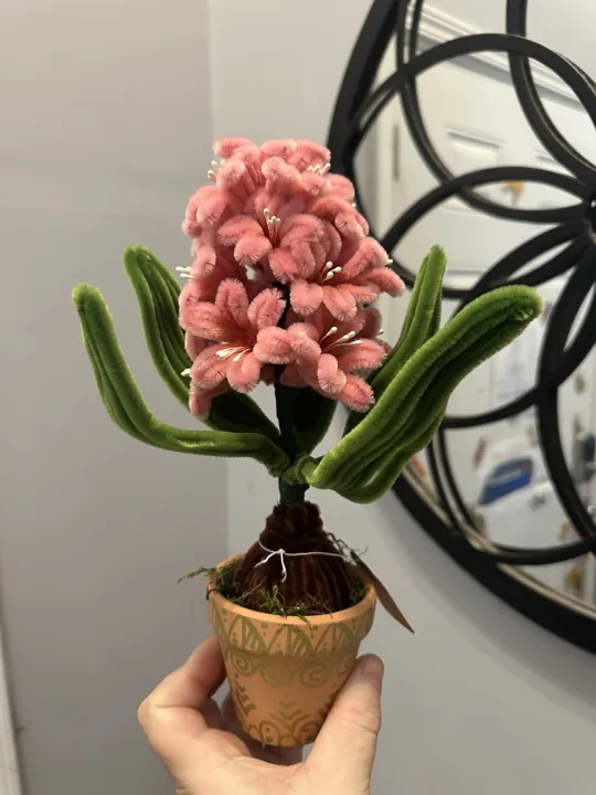 A pink wire-and-chenille hyacinth in a small terracotta pot, held up in one hand