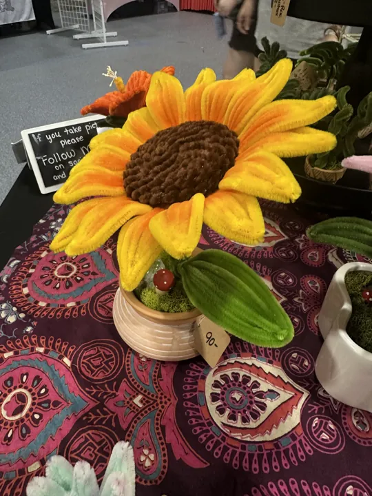 A large yellow-and-orange wire sunflower with a brown chenille center in a pale pot